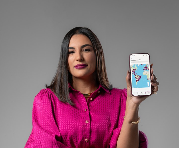 Audrey Olaia, fundadora, segurando o app Milhas Mágicas com o mapa do mundo